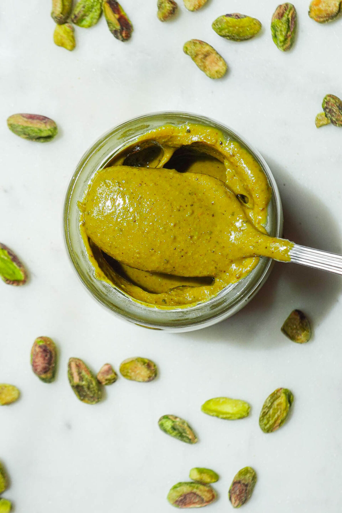 Vegan pistachio butter in a small glass jar on a marble background