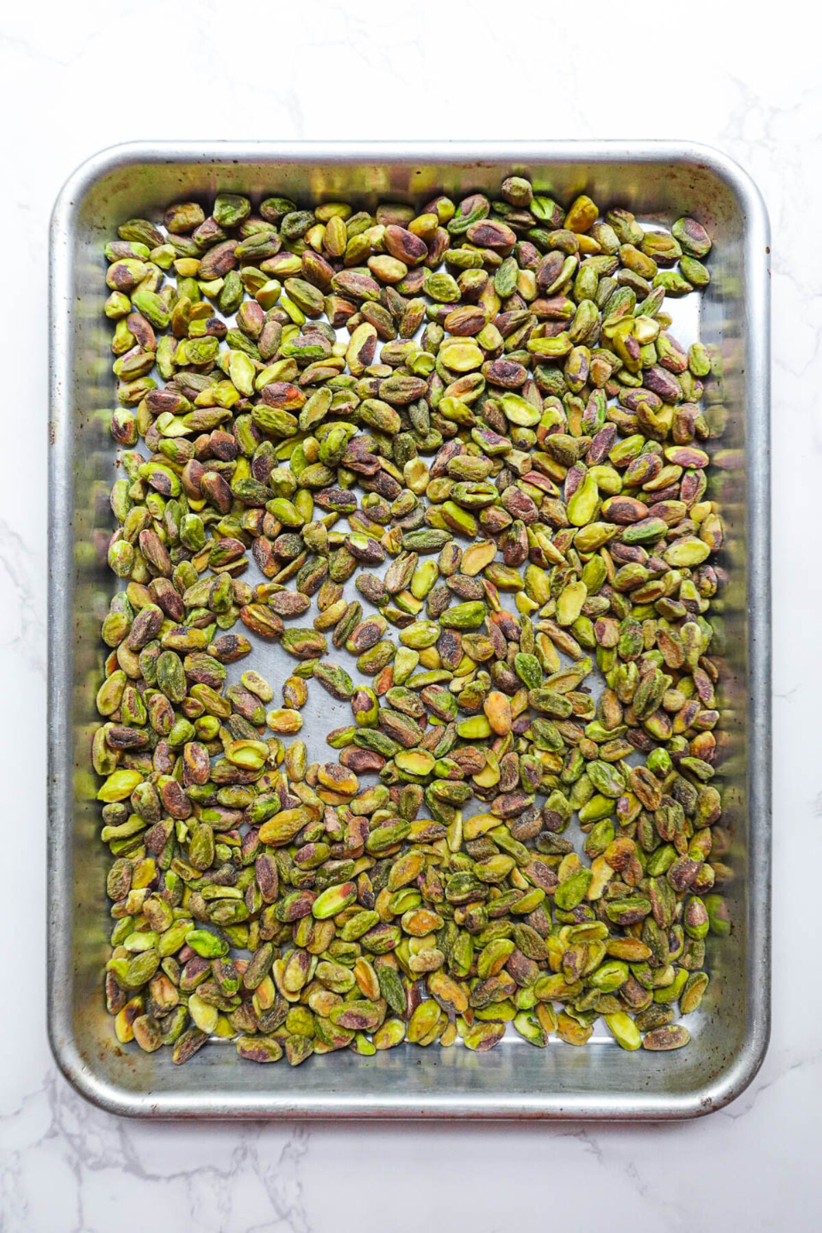 Raw shelled pistachios on a baking tray before roasting