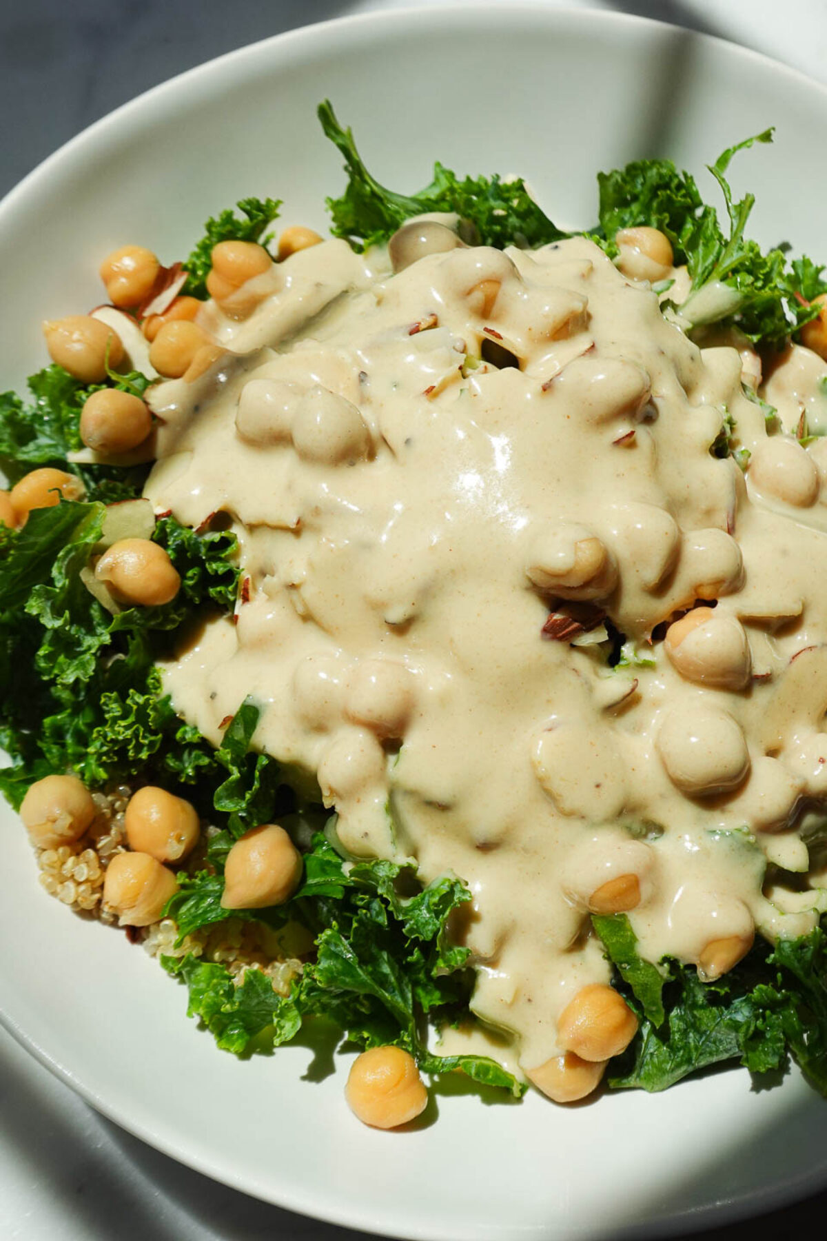 Pouring lemon tahini dressing over chickpea quinoa salad