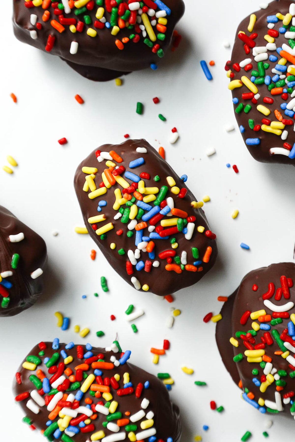 Cosmic brownie stuffed dates on a white plate with sprinkles scattered around.