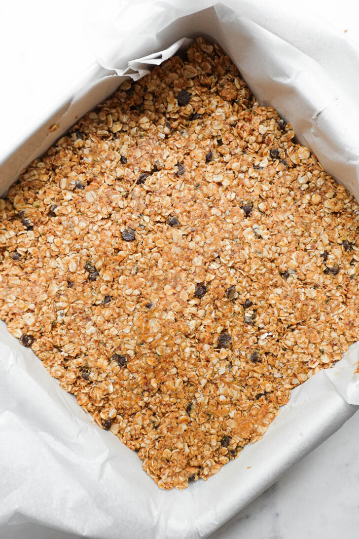 Granola bar mixture pressed into lined 8x8 pan before chilling