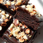 Close-up of gooey no bake brownies topped with chocolate ganache and crunchy hazelnuts