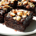 Side view of no bake vegan brownies with thick chocolate ganache layer and chopped hazelnuts on top