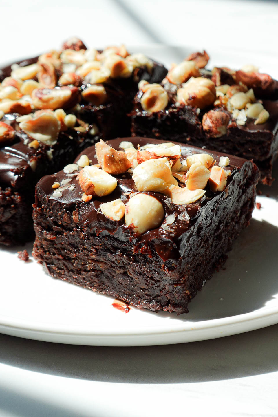 Side view of no bake vegan brownies with thick chocolate ganache layer and chopped hazelnuts on top