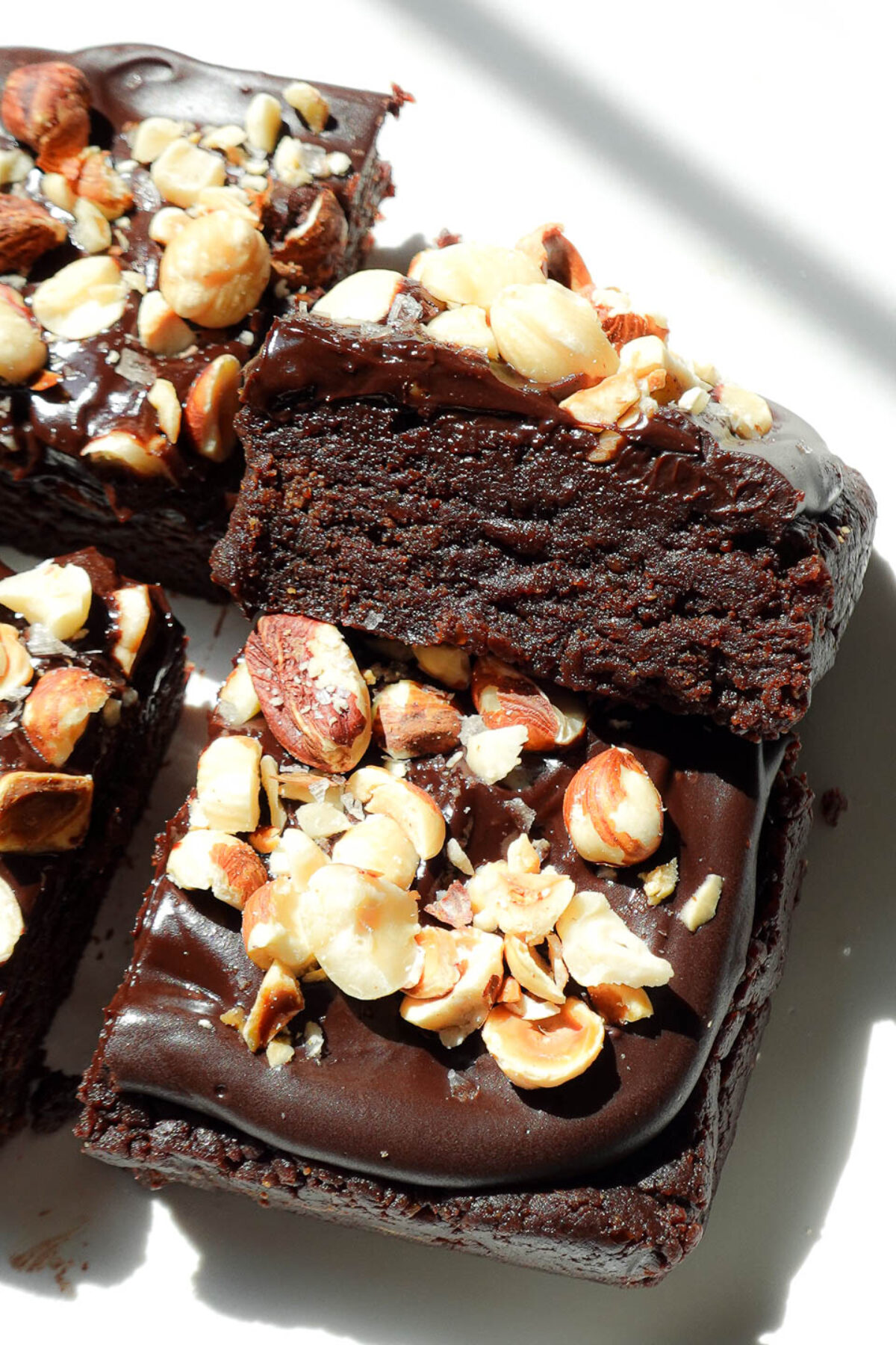 Close-up of fudgy, no-bake, healthy brownies topped with chocolate ganache and crunchy hazelnuts