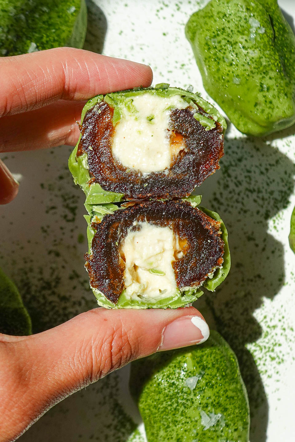 Holding vegan matcha stuffed date cut in half showing it's cheesecake-style yogurt filling
