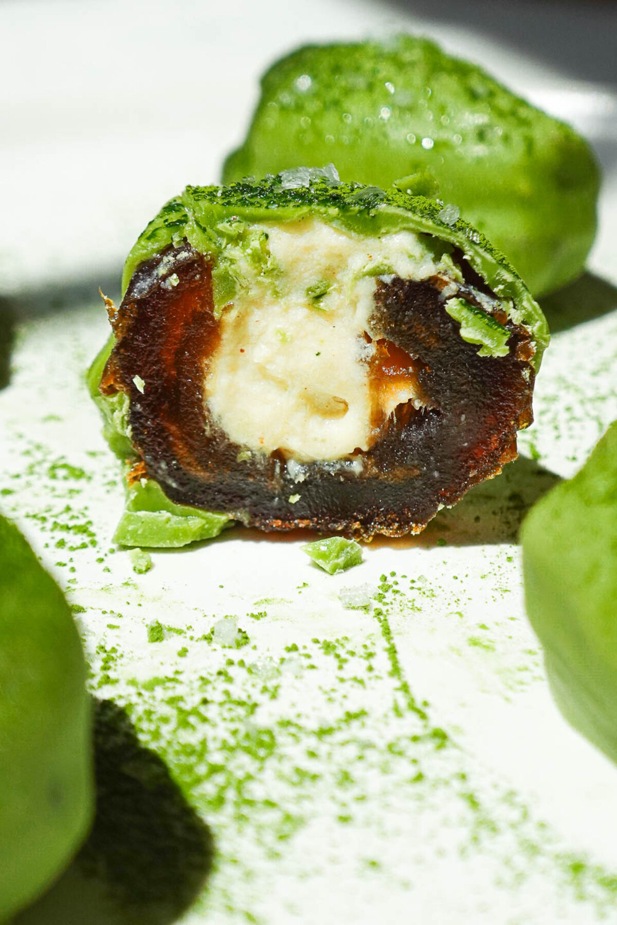 Matcha stuffed date cut in half showing creamy vegan yogurt filling and vibrant matcha white chocolate shell