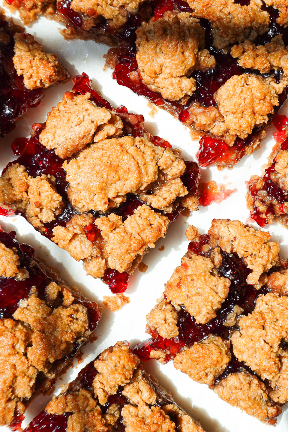 Healthy peanut butter and jelly bars sliced on parchment paper with jam oozing out