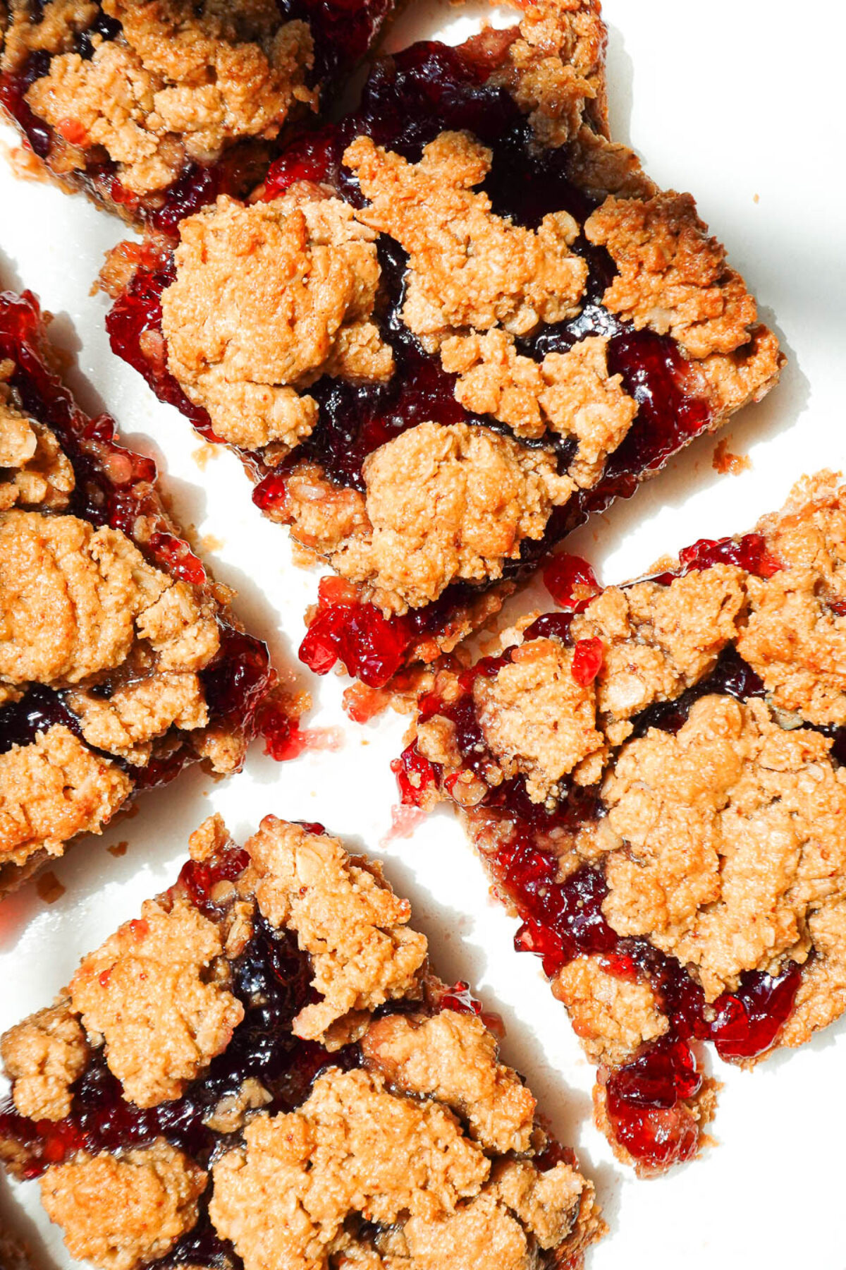 overhead shot of healthy peanut butter and jelly bars sliced on parchment paper with jam oozing out