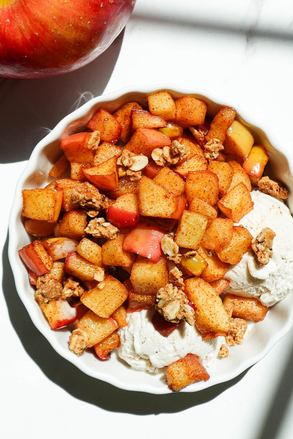 Bowl of warm cinnamon air fryer apples sprinkled with granola and served with vegan vanilla ice cream