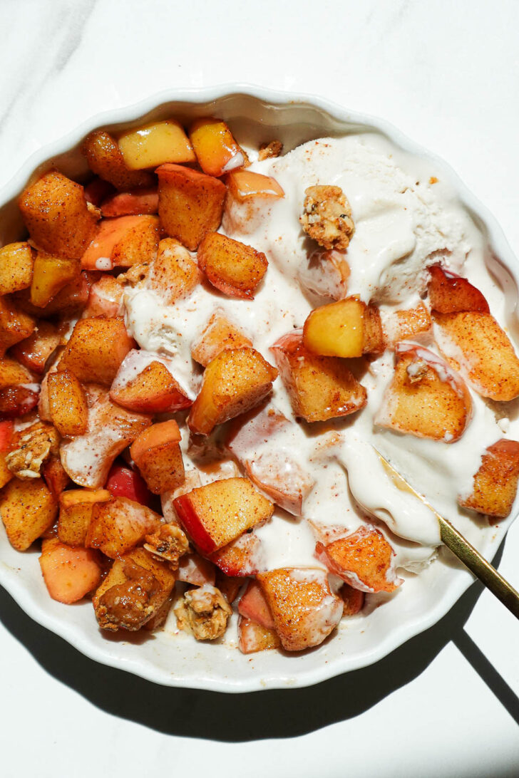 Healthy air fryer apples in a ramekin with melty vanilla ice cream and granola on top