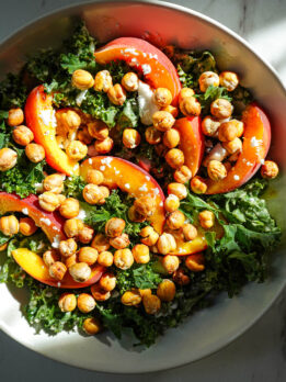 Bowl of kale salad with peaches, crispy chickpeas, vegan feta, and honey tahini dressing