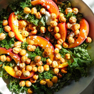 Bowl of kale salad with peaches, crispy chickpeas, vegan feta, and honey tahini dressing