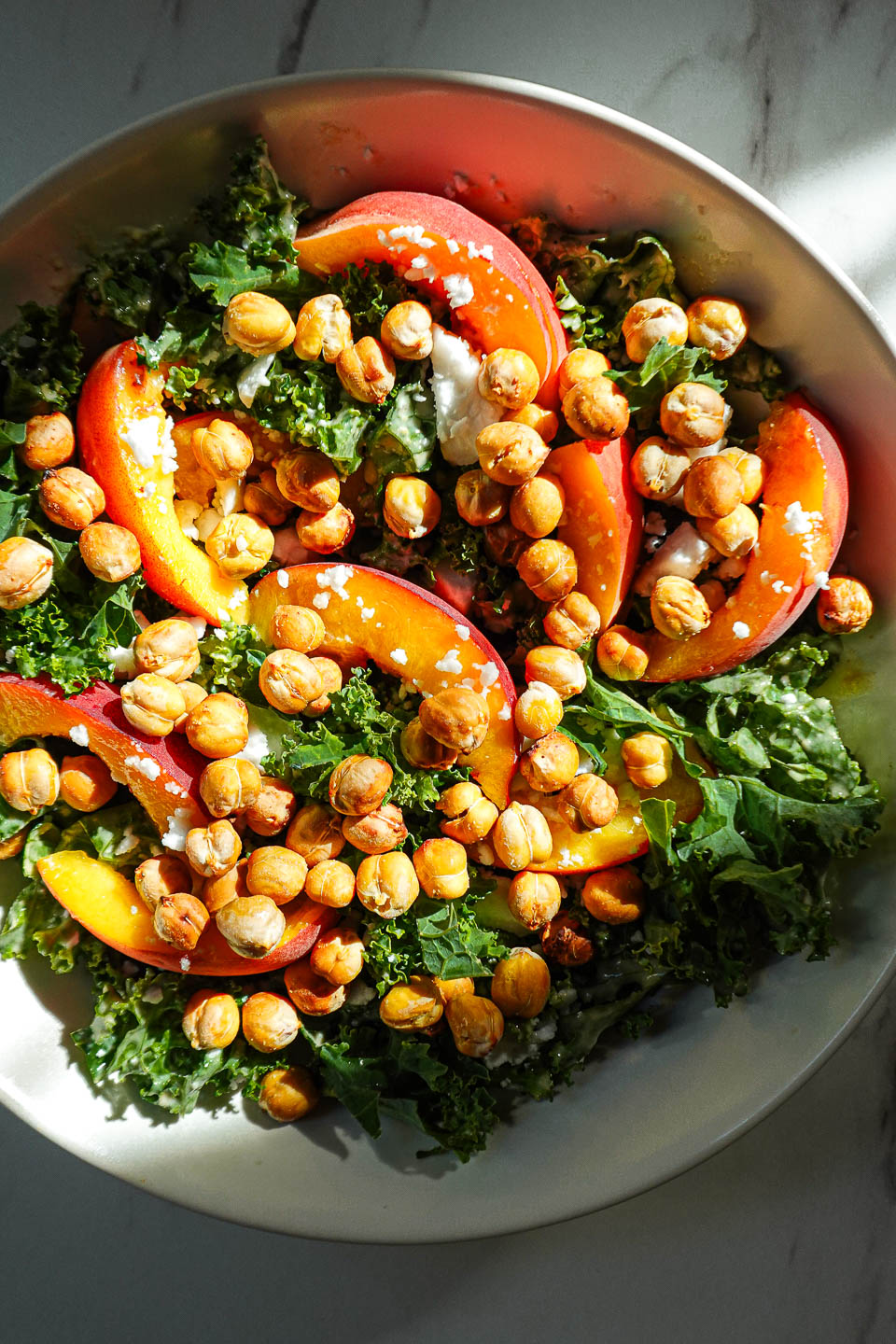 Bowl of kale salad with peaches, crispy chickpeas, vegan feta, and honey tahini dressing