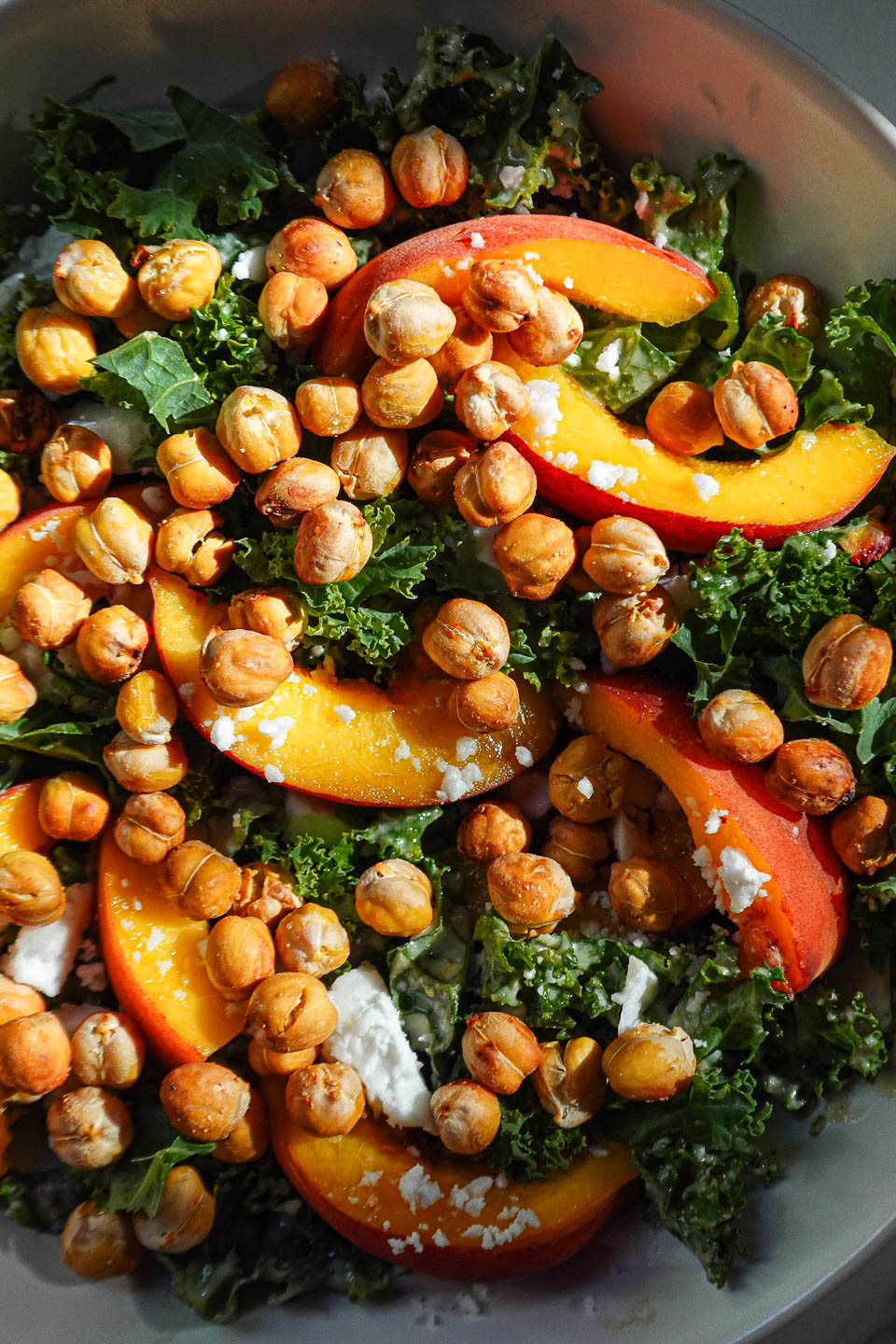 Close-up of peach kale salad topped with crispy chickpeas, vegan feta, fresh peaches, and a creamy tahini dressing