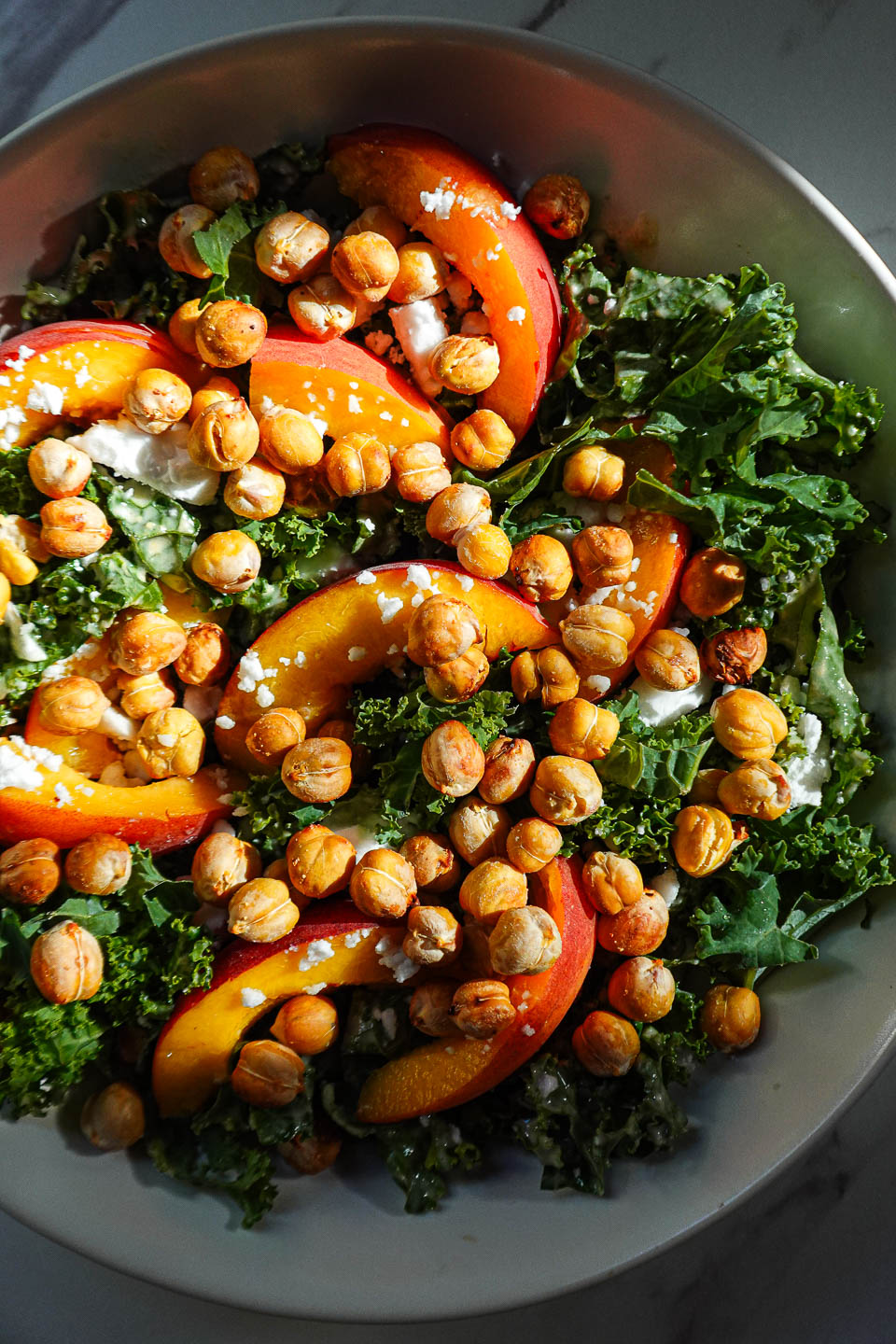 Bowl of kale salad with peaches, crispy chickpeas, vegan feta, and honey tahini dressing