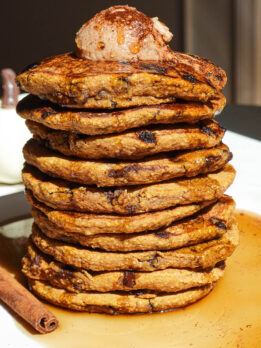 Stack of fluffy pumpkin chocolate chip pancakes topped with maple cinnamon butter and drizzled with maple syrup
