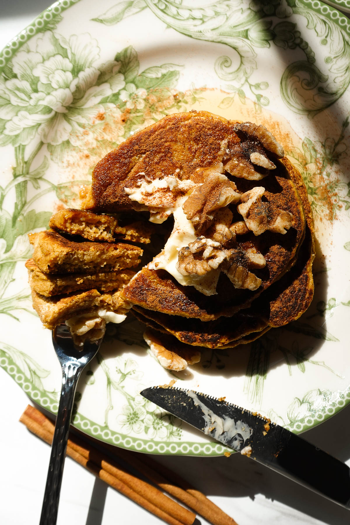 Stack of vegan pumpkin pancakes served with cinnamon butter, maple syrup, and chopped nuts.