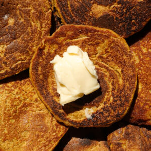 Close up of gluten-free pumpkin pancakes topped with vegan butter.
