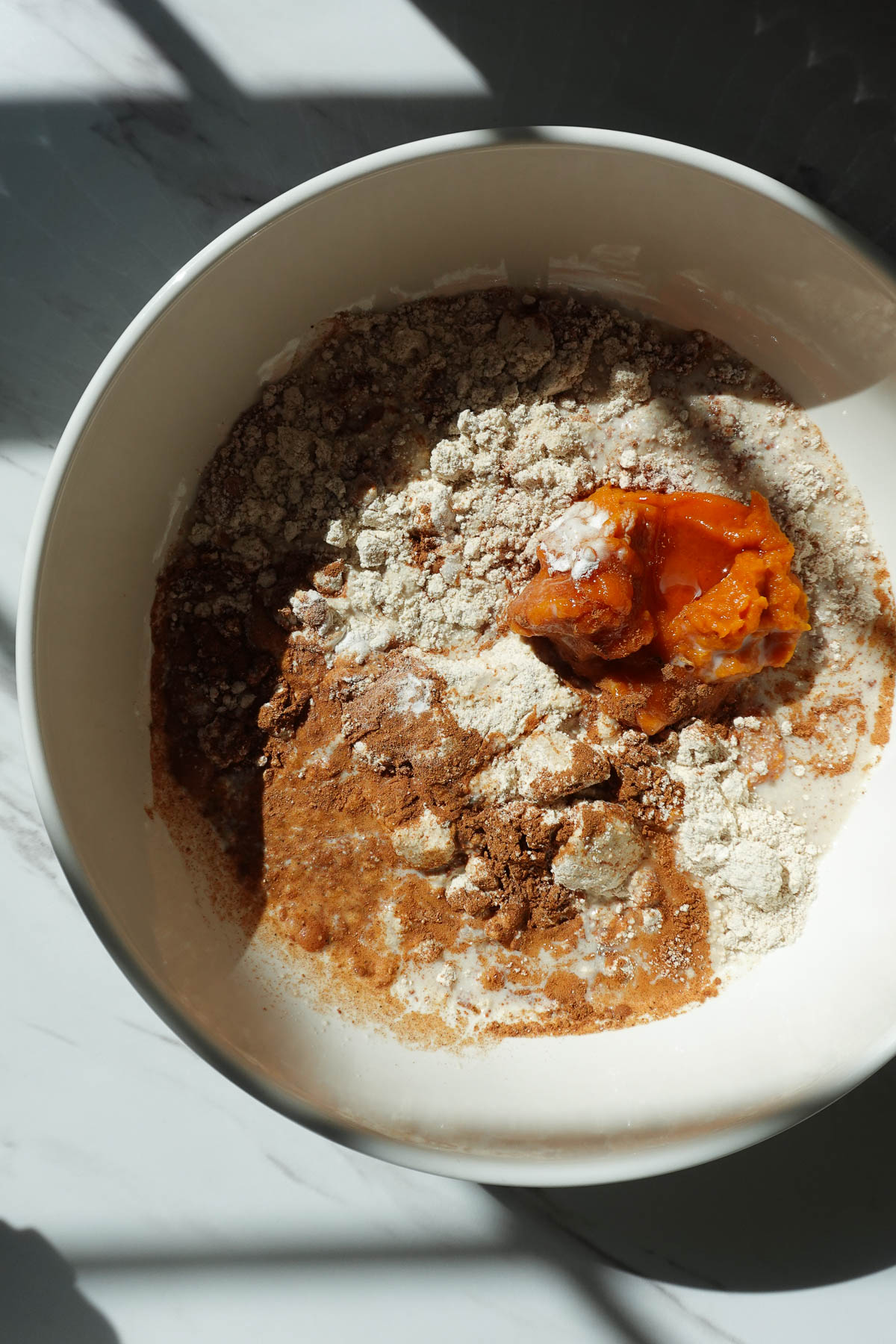 Oat flour, pumpkin puree, non-dairy milk, maple syrup, and spices in a mixing bowl.
