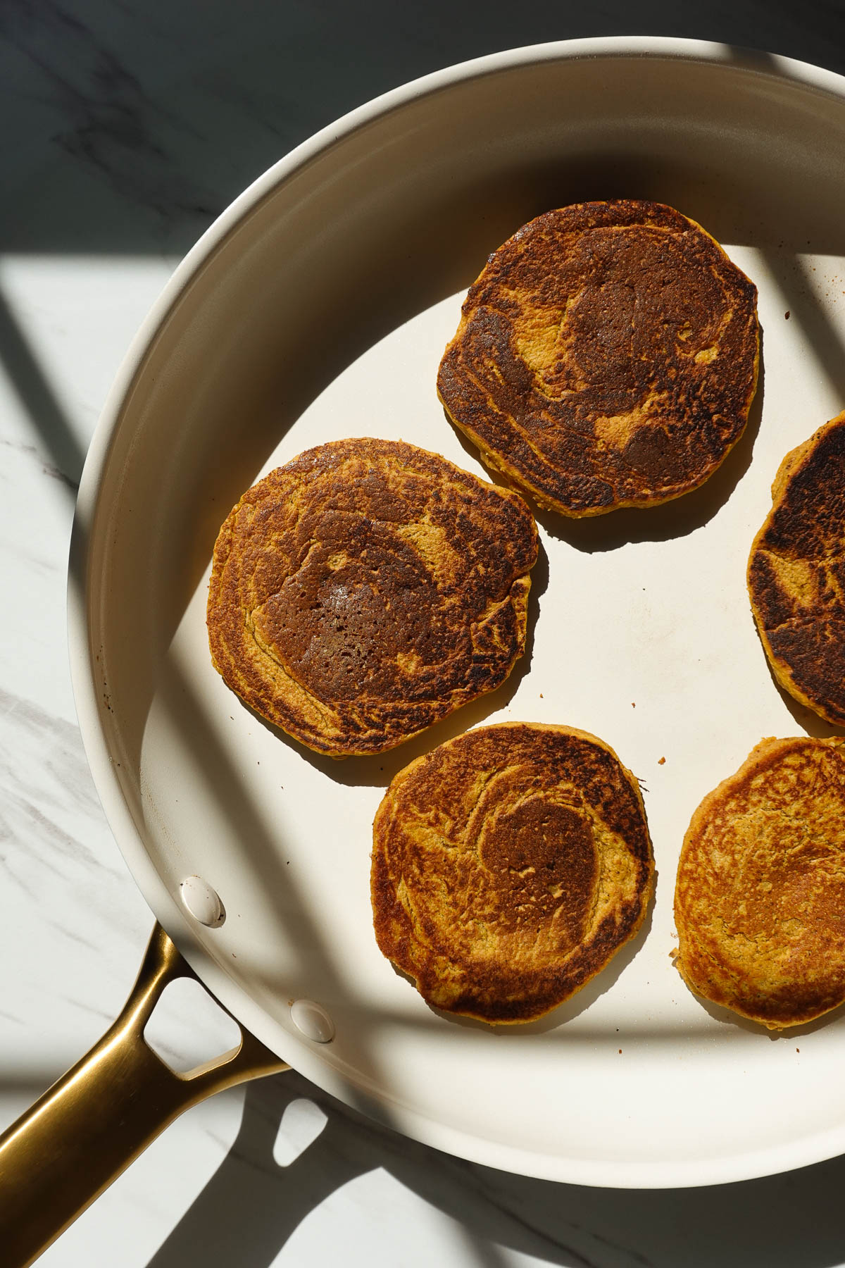 Vegan pumpkin pancakes cooking in a skillet.