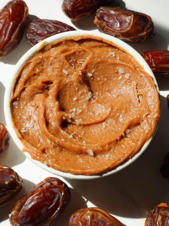 Healthy date caramel in a bowl surrounded by fresh dates and topped with flaky sea salt.