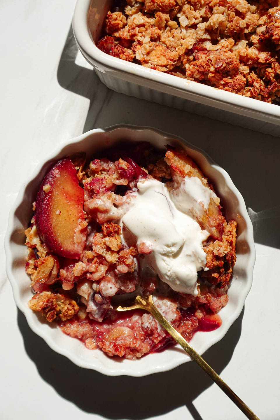 Close-up of healthy plum crisp topped with a scoop of vegan vanilla ice cream melting into the crisp