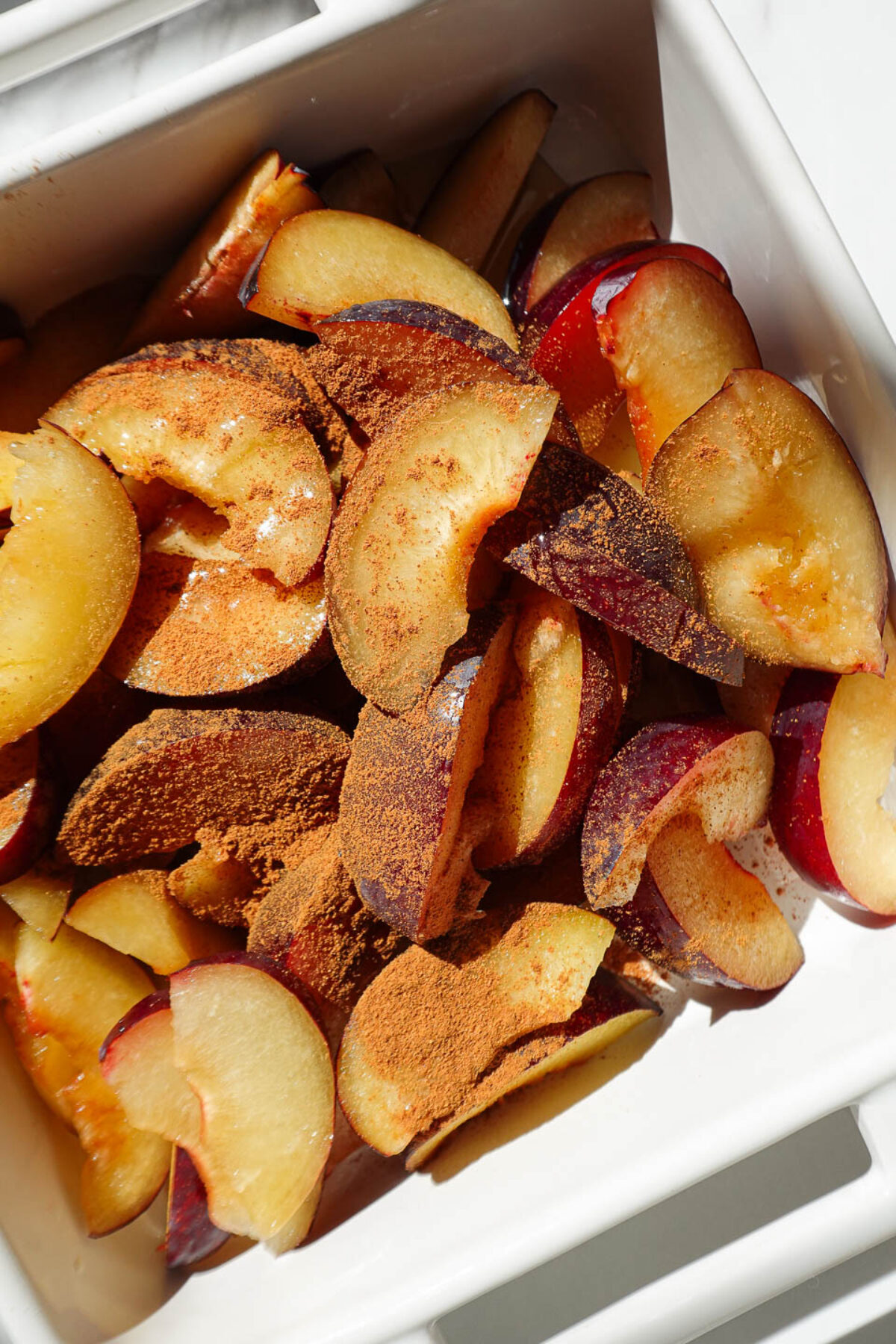 Sliced plums tossed with maple syrup and cinnamon in a mixing bowl for healthy plum crisp