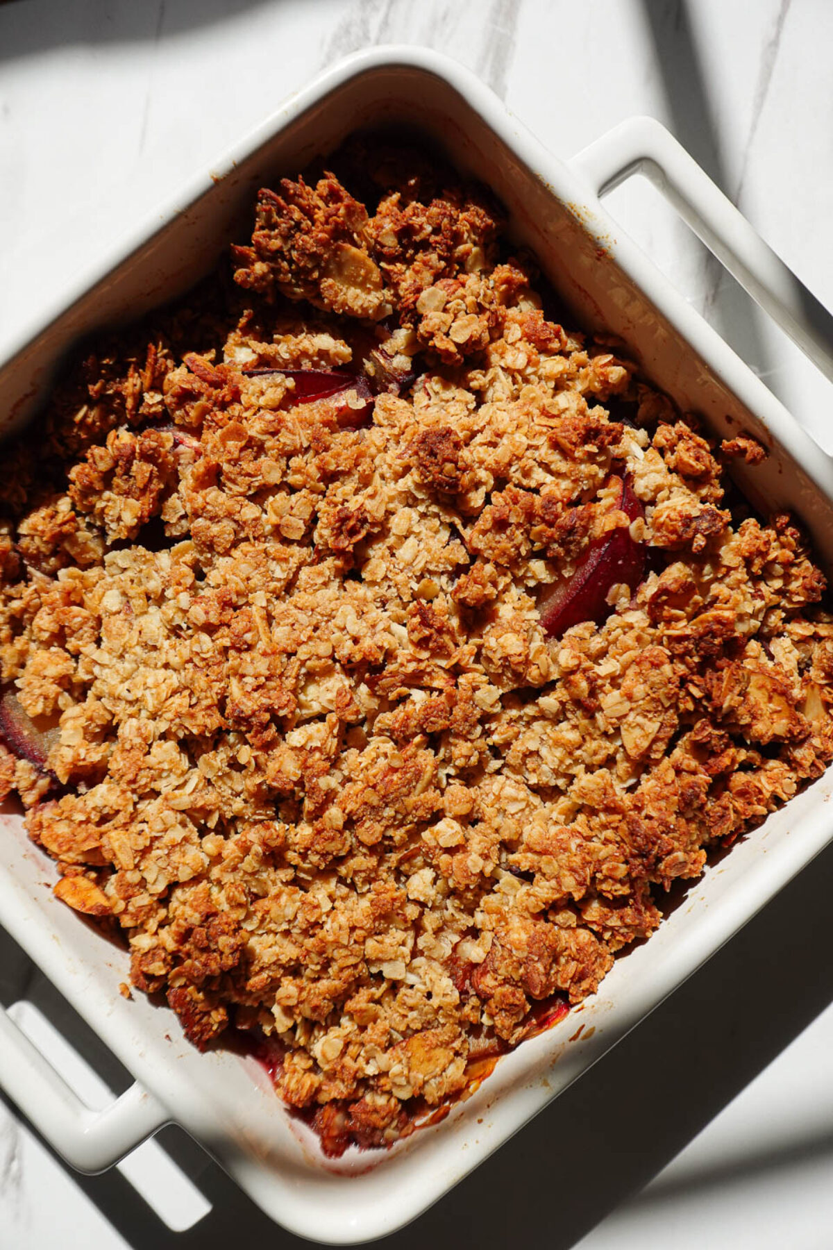 Freshly baked plum crisp with golden almond oat topping bubbling around the edges