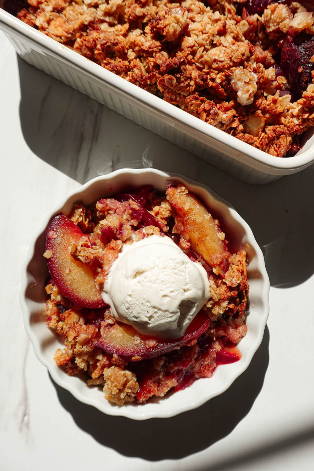 vegan plum crisp in a ramekin topped with a scoop of vanilla ice cream