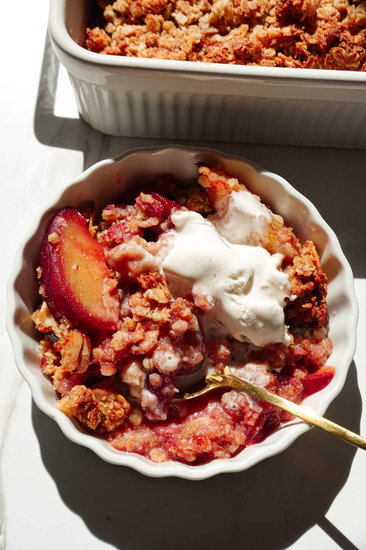Close-up of healthy plum crisp topped with a scoop of vegan vanilla ice cream melting into the crisp