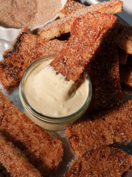 Close-up of a gingerbread French toast stick being dipped into creamy vanilla vegan yogurt