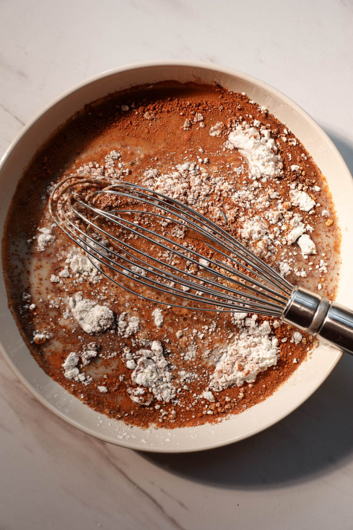 Whisking vegan gingerbread French toast batter with soy milk, maple syrup, flaxseed, and warm spices
