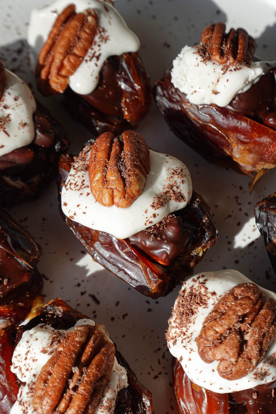 close up of pecan pie stuffed dates arranged on a plate with whipped cream and pecans on top