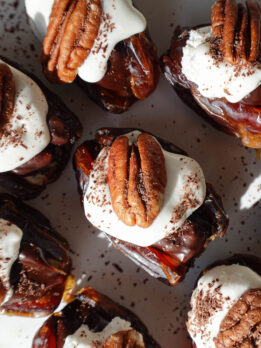 Pecan pie stuffed dates arranged on a plate with whipped cream and pecans on top