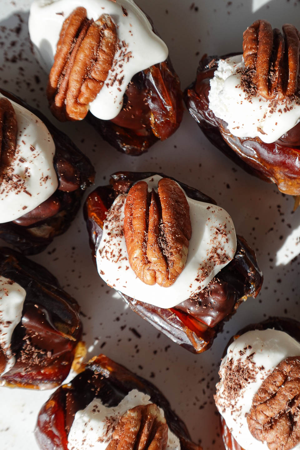 Pecan pie stuffed dates arranged on a plate with whipped cream and pecans on top