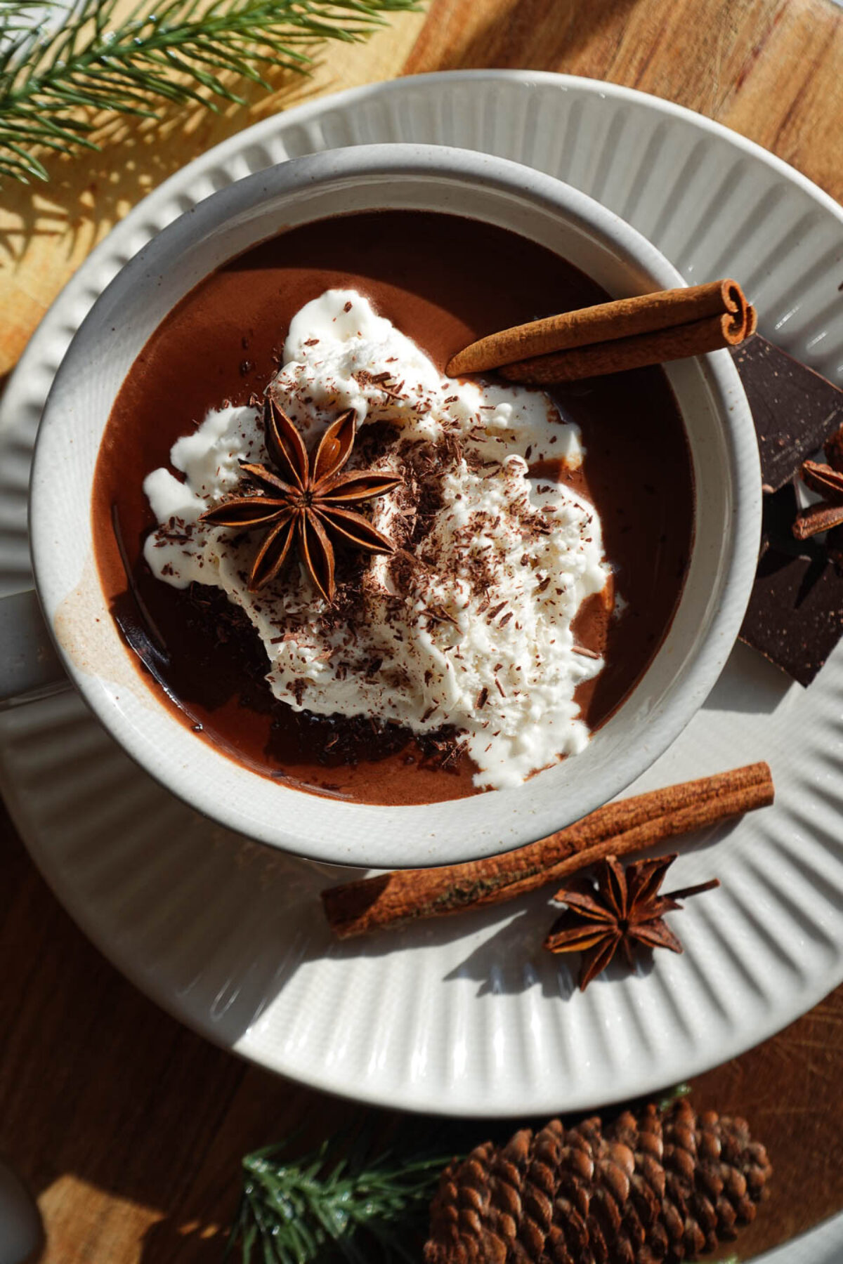 overhead shot of vanilla chai hot chocolate topped with non-dairy whipped cream, a cinnamon stick, a star anise pod, and shaved chocolate.