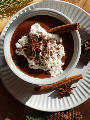 overhead shot of vanilla chai hot chocolate topped with non-dairy whipped cream, a cinnamon stick, a star anise pod, and shaved chocolate.