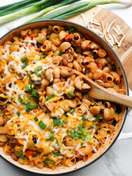 vegan chili mac and cheese made in one-pot and topped with melted vegan cheese and scallions with a wooden spoon