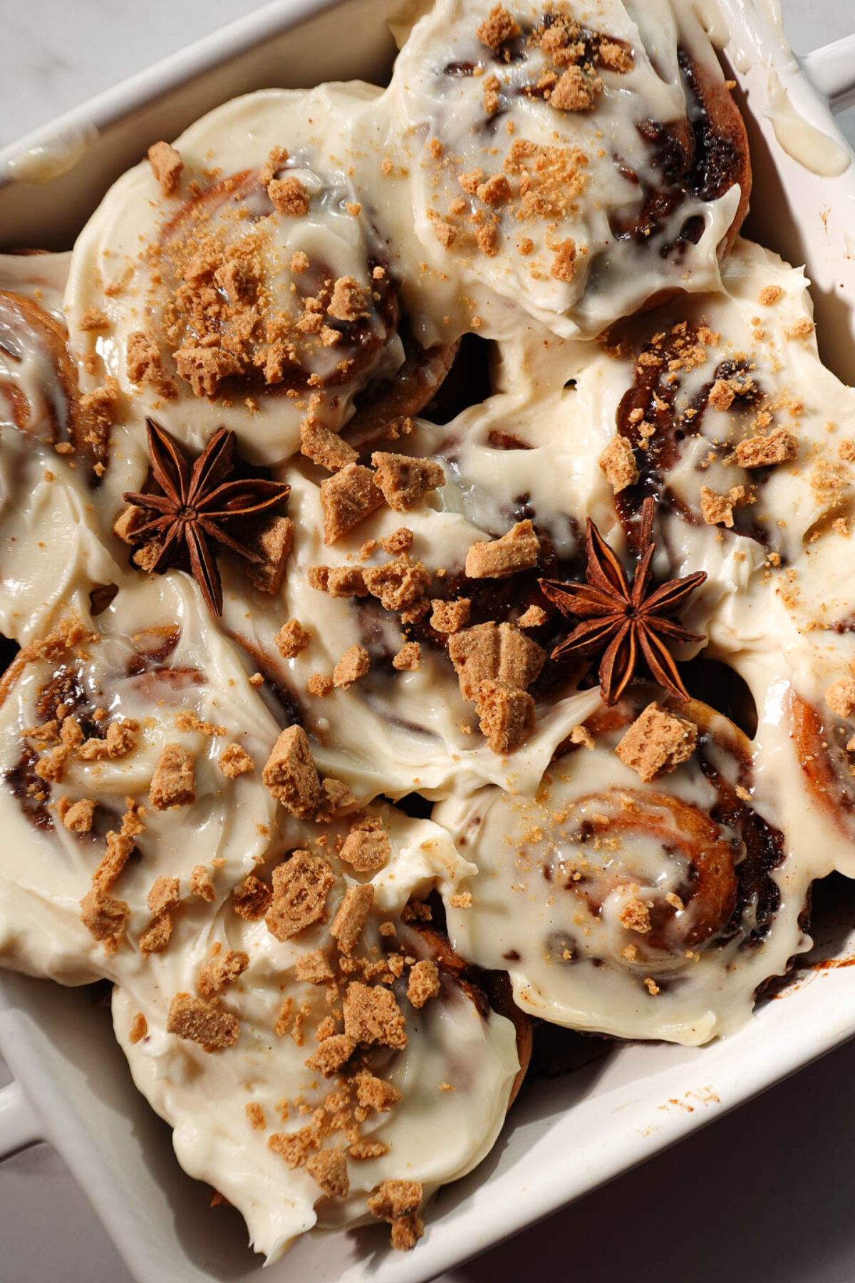 Close-up of gingerbread cinnamon rolls showing tight, defined swirls and creamy cream cheese frosting topped with crushed graham crackers and star anise pods