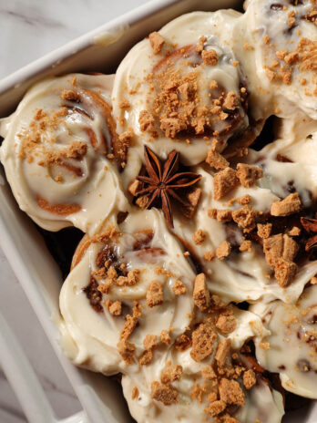 Close-up of gingerbread cinnamon rolls showing tight, defined swirls and creamy cream cheese frosting topped with crushed graham crackers and star anise pods