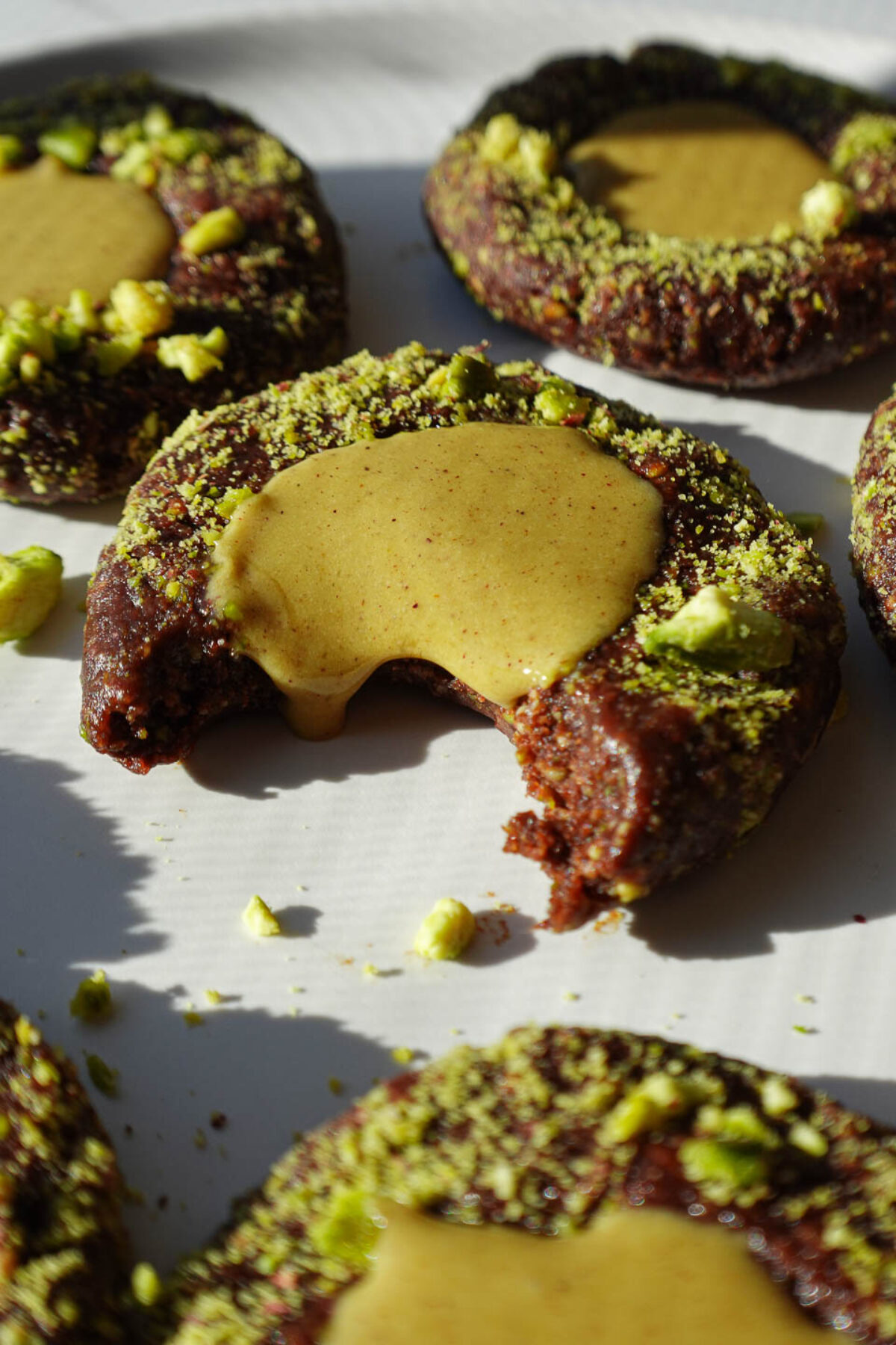 Close-up of a no-bake pistachio thumbprint cookie showing the chocolate base and pistachio filling dripping out