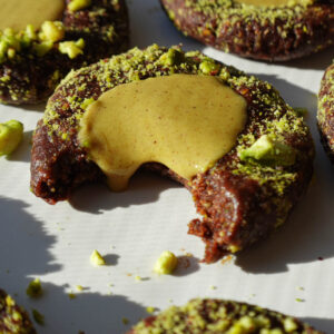 Close-up of a no-bake pistachio thumbprint cookie showing the chocolate base and pistachio filling dripping out