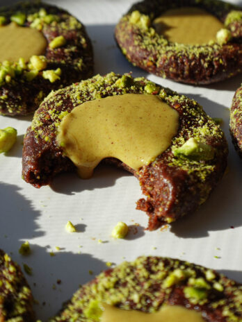 Close-up of a no-bake pistachio thumbprint cookie showing the chocolate base and pistachio filling dripping out