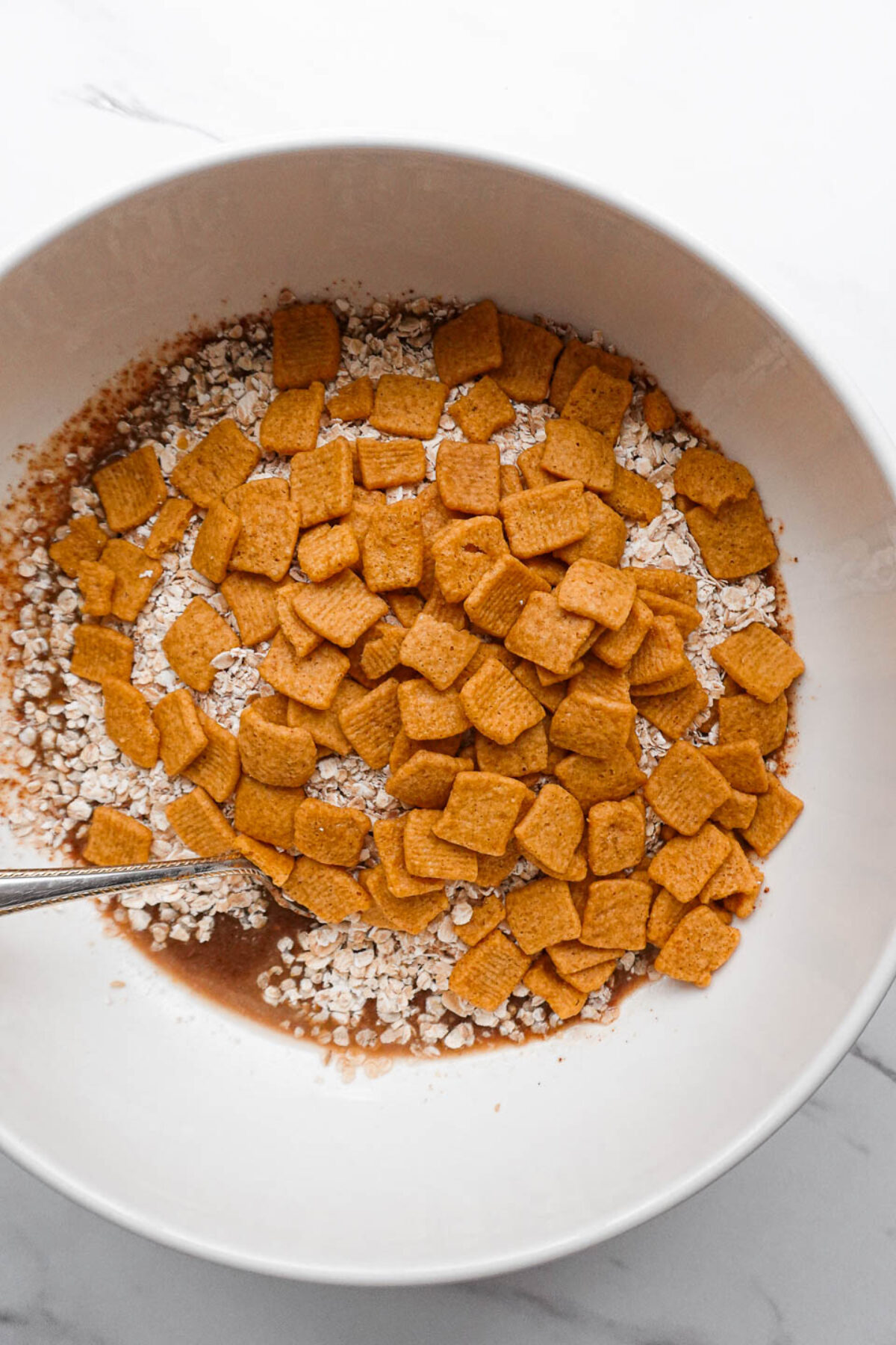Vegan cinnamon toast crunch granola being mixed in a bowl before baking.