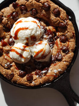 vegan and gluten-free chocolate chip skillet cookie dessert served straight from the skillet with vanilla ice cream on top