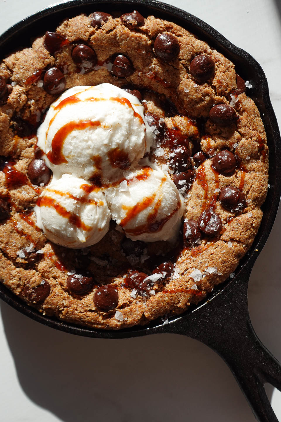 vegan and gluten-free chocolate chip skillet cookie dessert served straight from the skillet with vanilla ice cream on top
