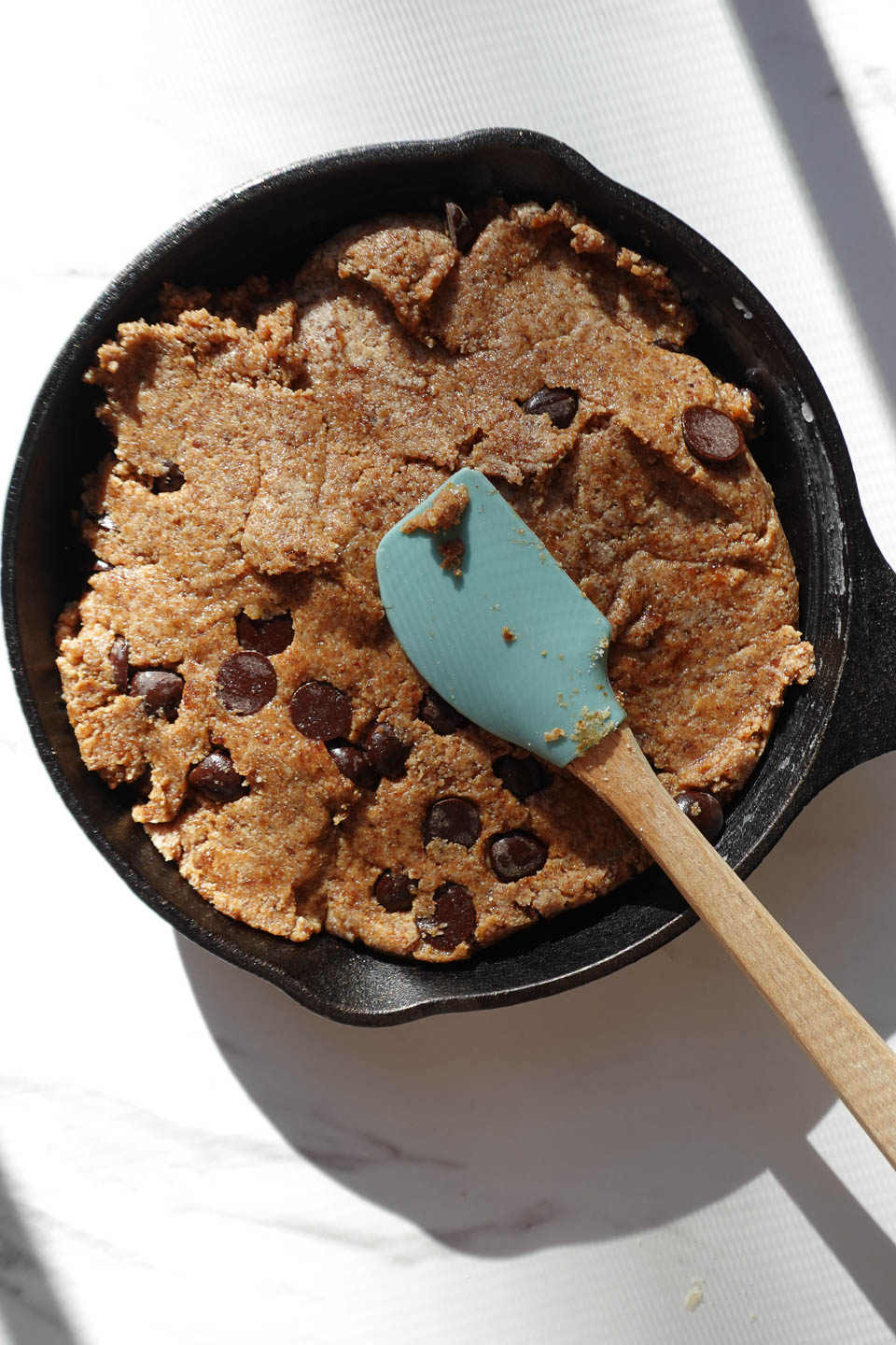 Pressing chocolate chip cookie dough evenly into a cast iron skillet
