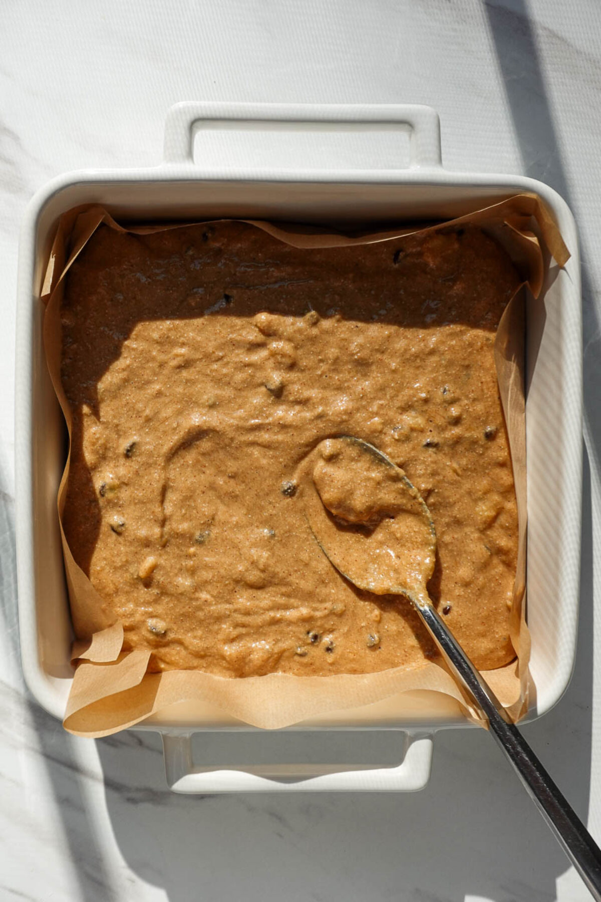 Spreading batter for vegan banana bars in a parchment-lined square baking pan before baking.