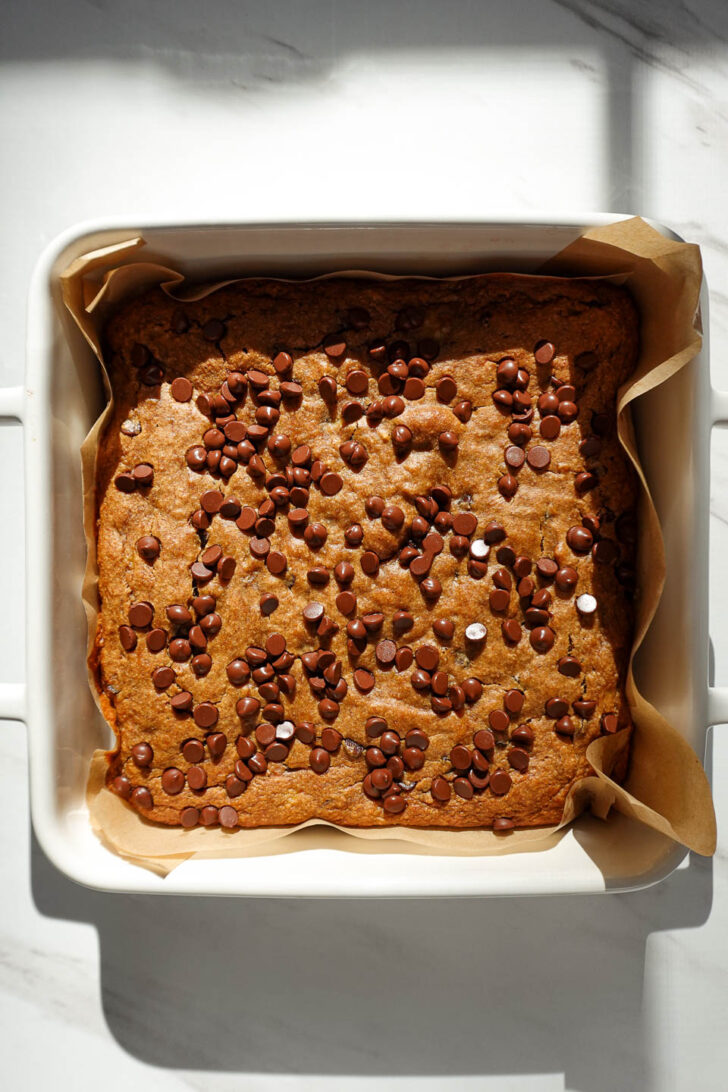 Freshly baked vegan chocolate chip banana bars in an 8x8 pan, golden on top with melted chocolate chips.